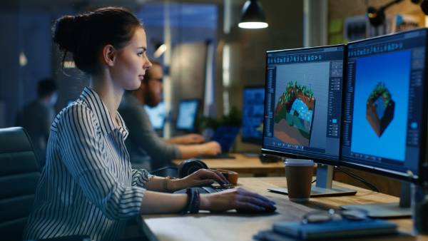 A female Game Developer Working on a Level Design on her computer along with other developers sitting beside her.